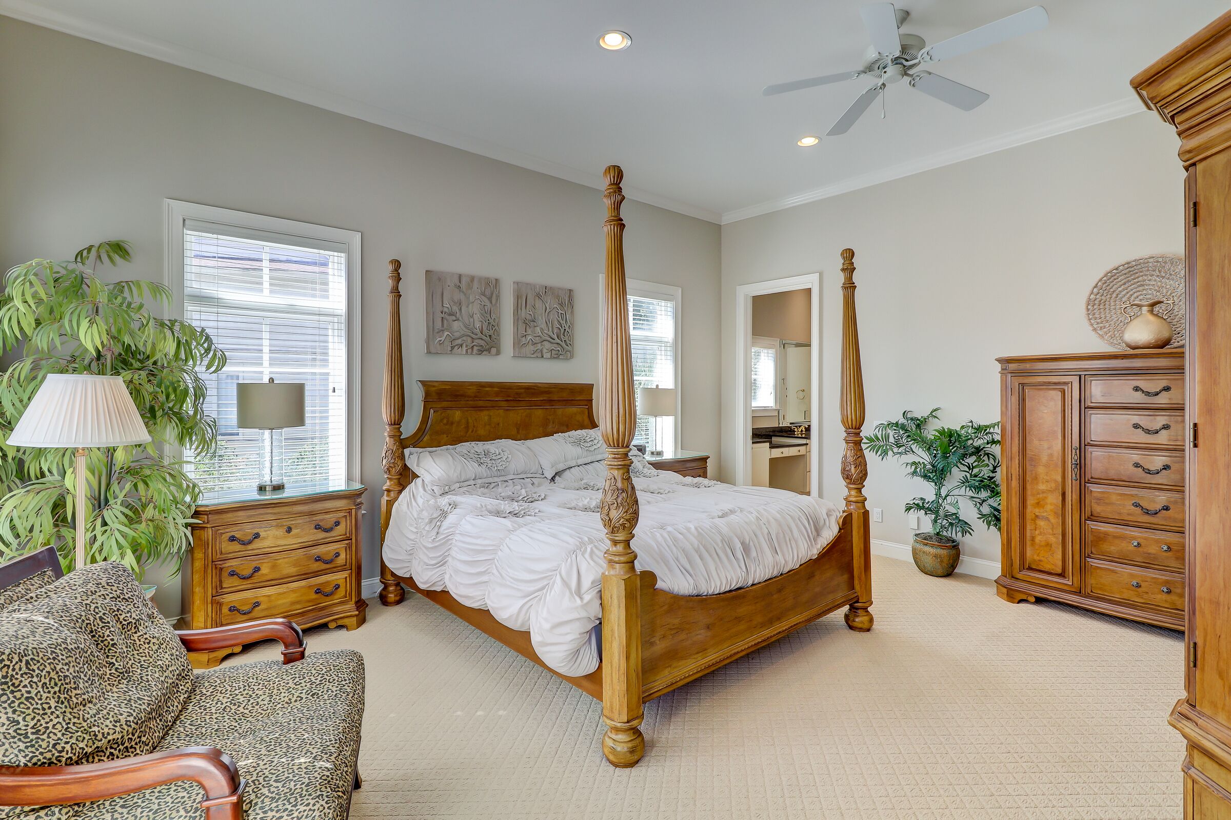 A four-poster bed with a wooden headboard, a wooden nightstand with drawers, a leopard-print armchair, a floor lamp, and a large potted plant.