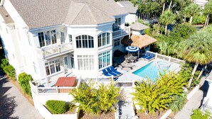 A large two-story house with a swimming pool, outdoor seating, and a thatched-roof structure. - 2nd Row luxury home with pool, tiki bar, private beach boardwalk- 30 Knotts Way (Hilton Head Island)