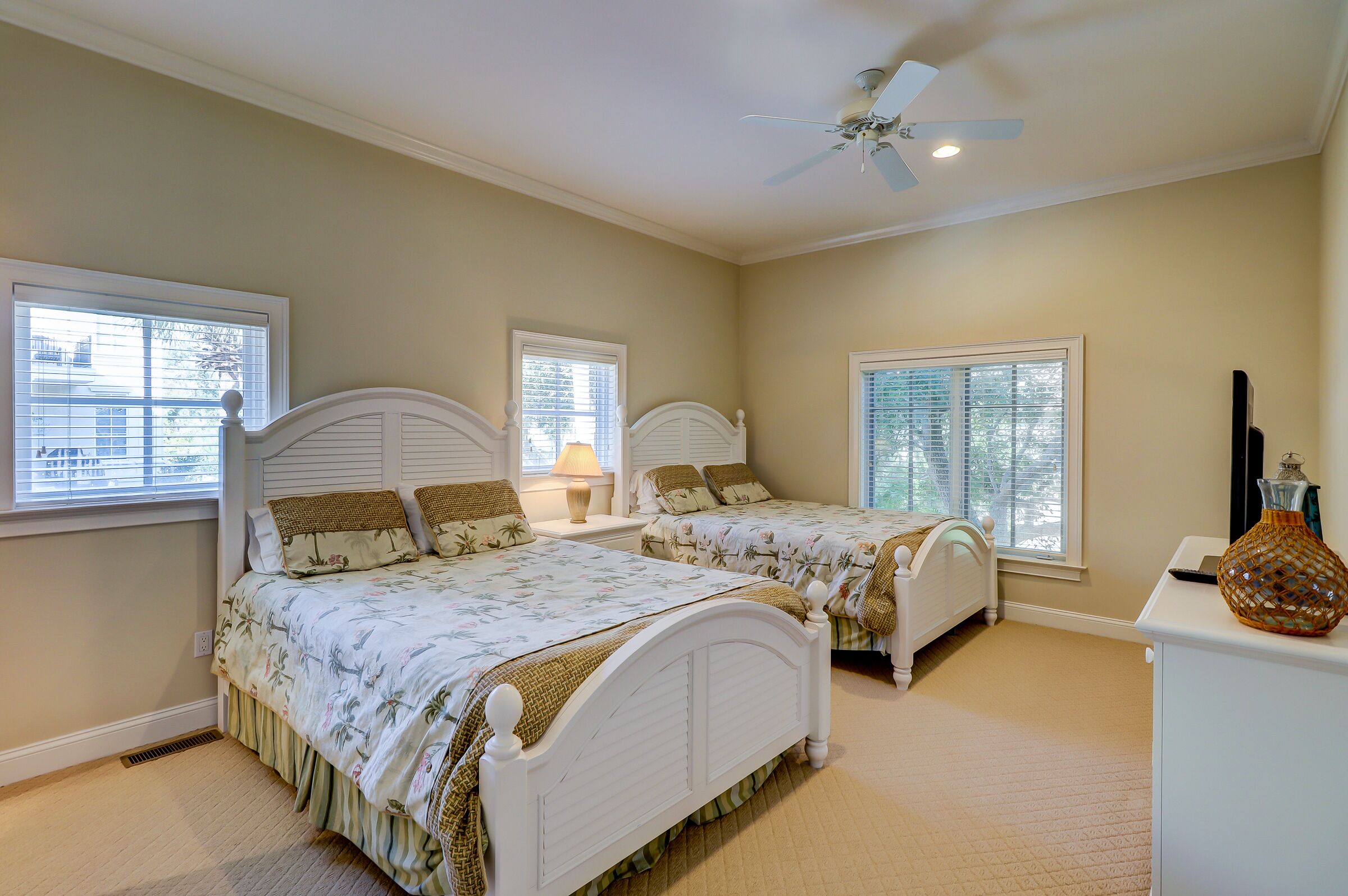 Une chambre avec deux lits blancs, un ventilateur de plafond et une petite commode blanche.