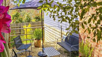 Eine Terrasse mit zwei Metallstühlen und einem kleinen Tisch, umgeben von Blumentöpfen und einem Holzzaun.