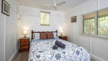 A bedroom with a wooden bed, two bedside tables with lamps, a ceiling fan, and a window with blinds.