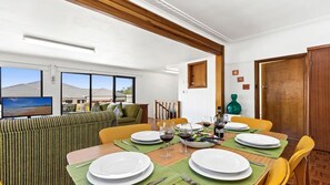 Enjoy meals with a view of the beach from this dining area, featuring a large window and comfortable seating.