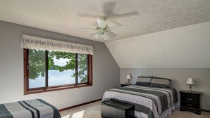 Un dormitorio con un ventanal grande, una cama, una mesita de noche, un banco y un ventilador de techo.