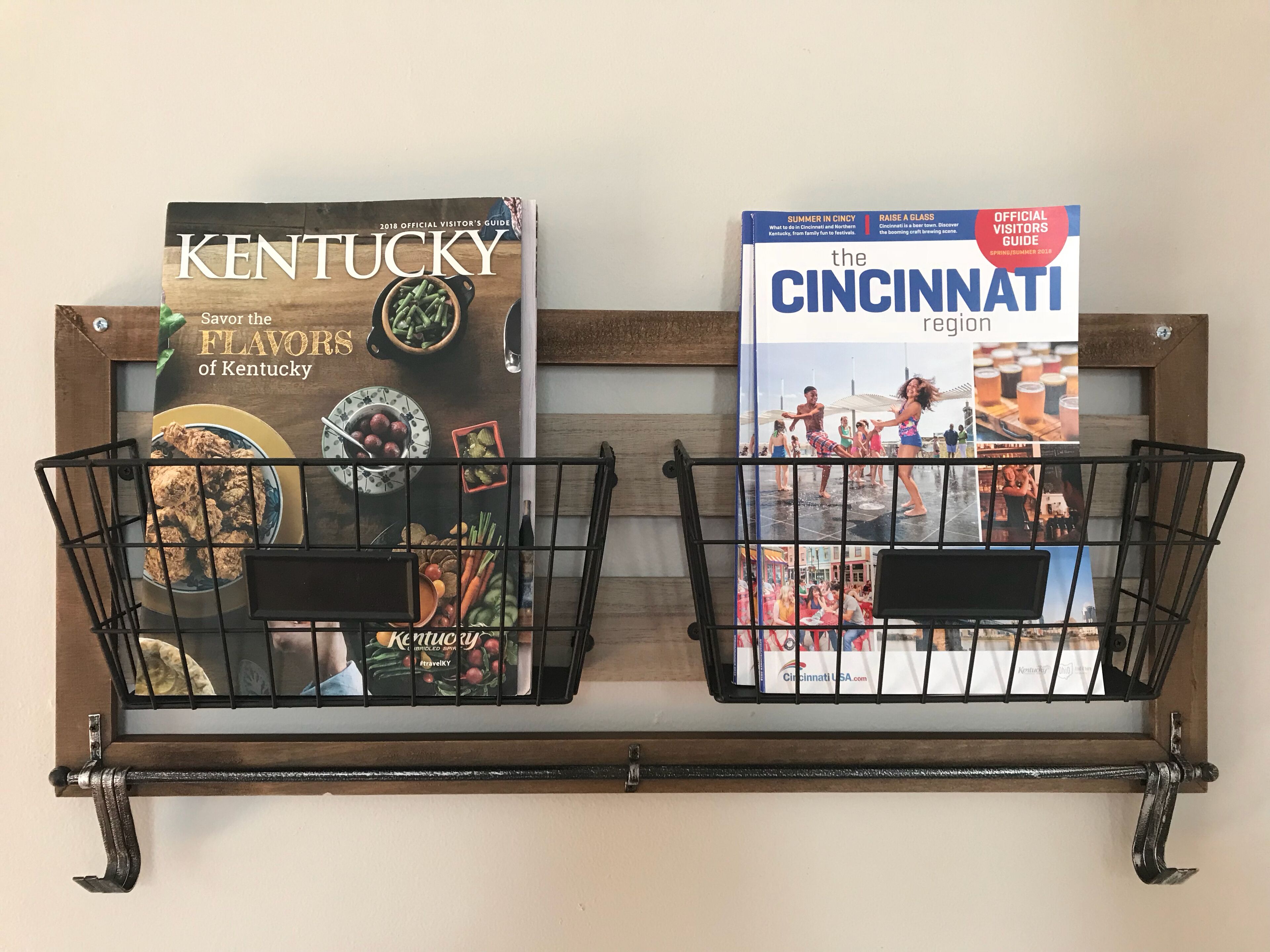 Two travel guides, 'Kentucky' and 'Cincinnati', displayed on a shelf with metal wire baskets.