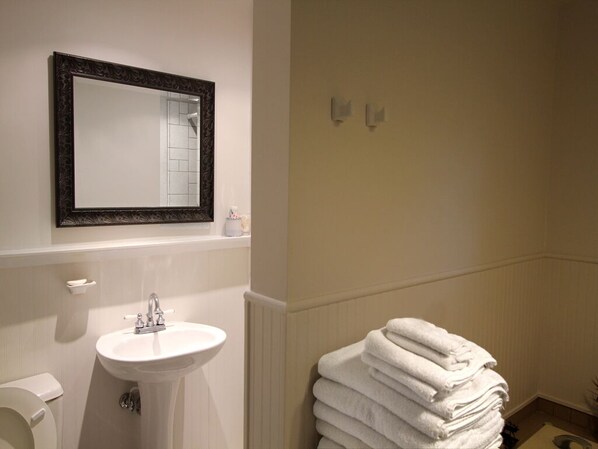 A bathroom with a white sink, a mirror with a dark frame, and a stack of white towels on the floor.
