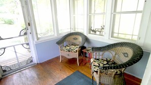 Une pièce lumineuse, baignée de soleil, avec de grandes fenêtres, des meubles en osier et un plancher en bois.