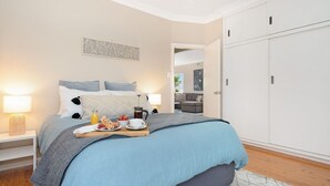 Een slaapkamer met een bed, nachtkastjes, een kledingkast en uitzicht op een andere kamer.