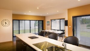 Een moderne keuken met een groot eiland, een eethoek met een tafel en stoelen, en grote ramen met uitzicht op de omgeving.