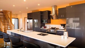 Een moderne keuken met donkere kastjes, een roestvrijstalen koelkast, een magnetron en een gasfornuis. Er is een witte aanrecht met een spoelbak en een afwassysteem.