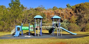 Ein Spielplatz mit Rutschen und Klettergerüsten, umgeben von Bäumen und einem felsigen Hintergrund.