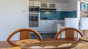 Una cocina compacta con armarios blancos, un salpicadero azul y un comedor con mesa y sillas de madera.