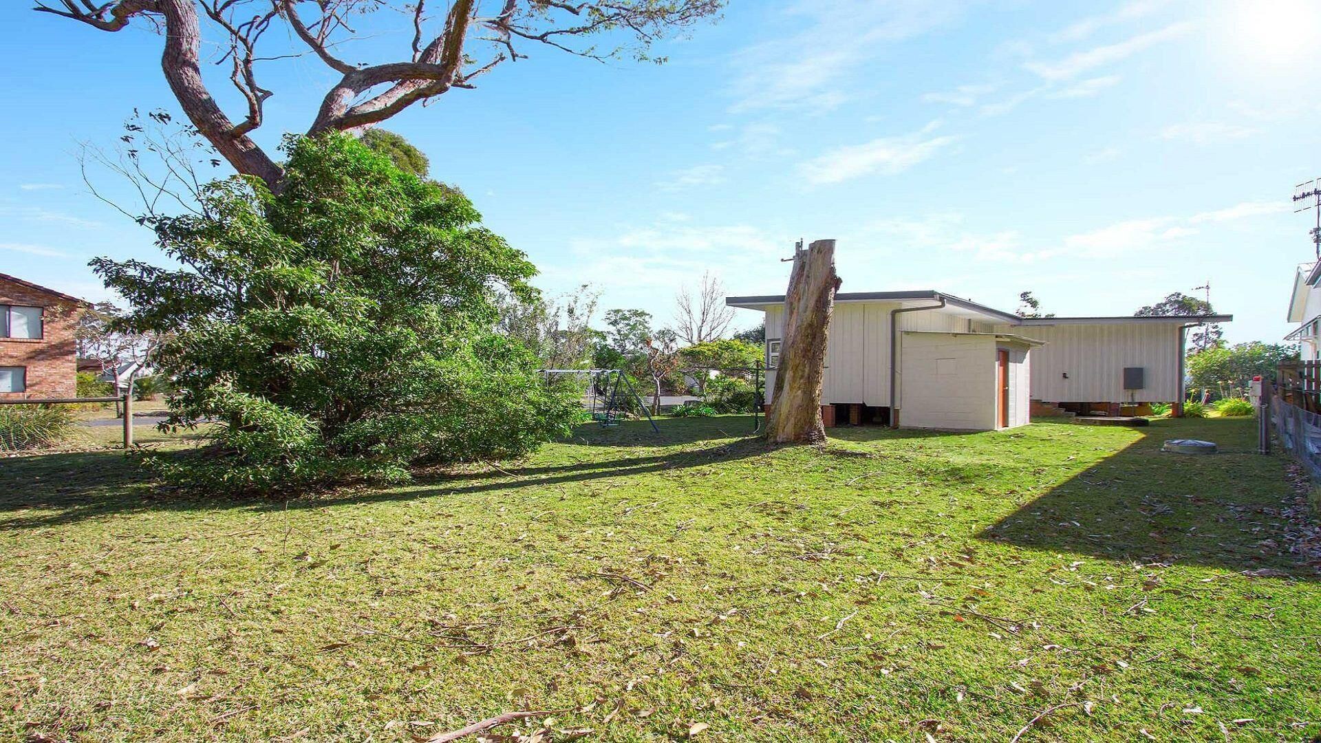 A residential property with a grassy yard, a large tree, and a small building with a garage.