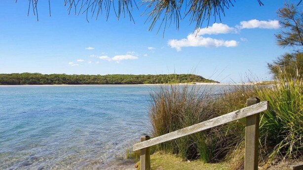 A wooden walkway leading to a beach with clear water and a forested hill in the background. - Bij's on the Beach – walking distance to beach (Lake Conjola)