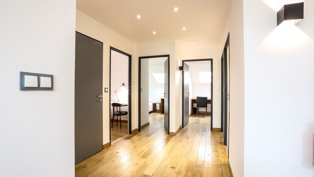 Een moderne hal met houten vloer, witte wanden en meerdere deuren die naar verschillende kamers leiden.