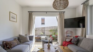Een moderne woonkamer met twee grijze banken, een salontafel en een televisie. Er is een balkon met een houten hek en tuinmeubilair.