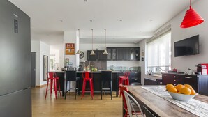 Een moderne keuken met een centraal eiland, rode barstoelen en een houten eettafel met een schaal mandarijnen.