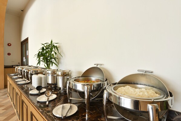 A buffet setup with various food containers, including rice and a vegetable dish, on a marble countertop.