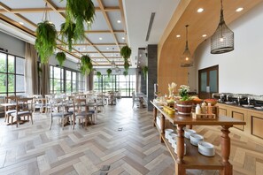 A spacious dining area with wooden tables and chairs, hanging plants, and a buffet setup.