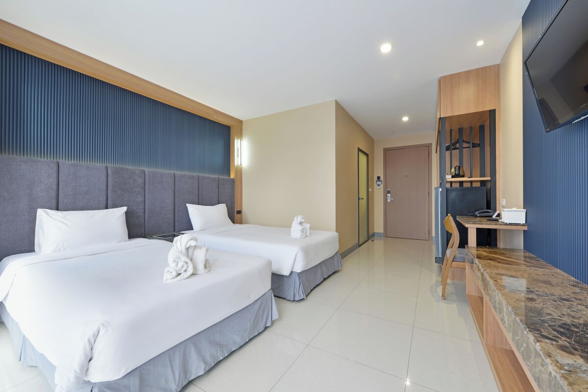 A hotel room with two beds, a desk, and a television.