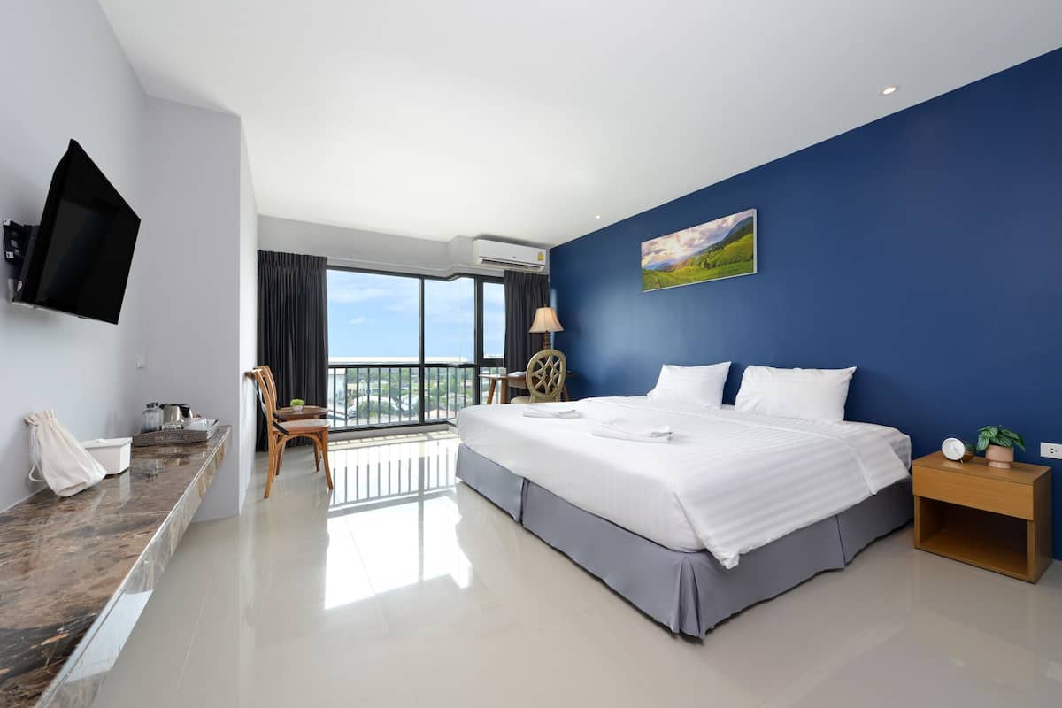 A hotel room with a large bed, a flat-screen TV, a balcony with a view, and a painting on the wall.
