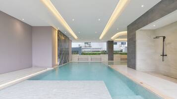 Una piscina interior moderna con vistas despejadas del entorno, que incluye un edificio con unidades de aire acondicionado y un jardín ajardinado.