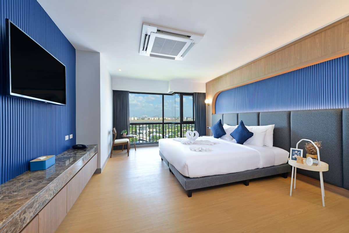 A modern hotel room with a large bed, a TV mounted on the wall, and a balcony with a city view.