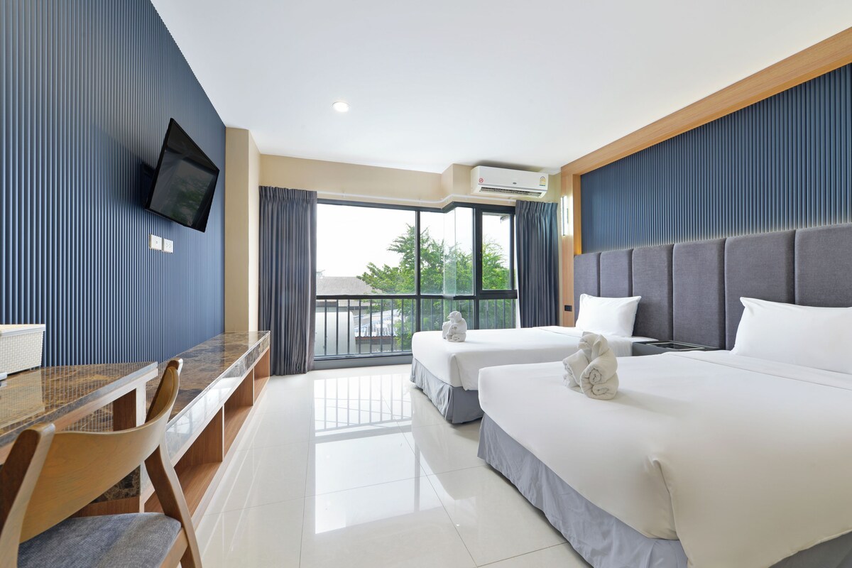A hotel room with a desk, two beds, a television, and a large window.