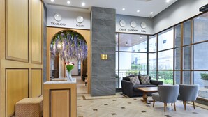 Un vestíbulo moderno con una recepción, un área de descanso con sofá y sillones, y ventanas amplias con vistas al exterior.