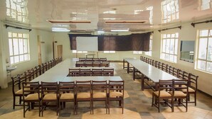 A large conference room with long tables and chairs, large windows, and a whiteboard. - Heritage Bliss Hotel (Kitui)