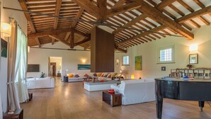Àmplia zona d'estar amb bigues de fusta al sostre, un sofà gran, una taula de centre i un piano.