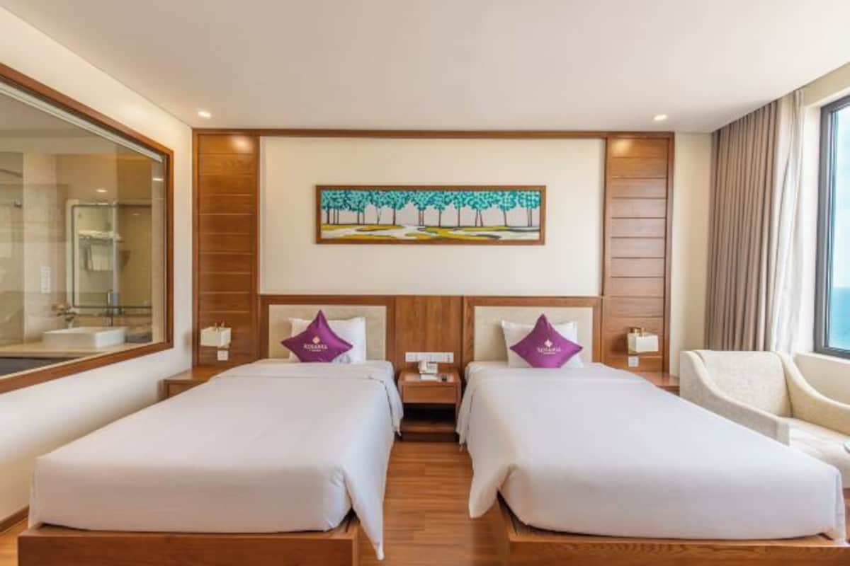 Une chambre d’hôtel avec deux lits, un tableau au mur, une fenêtre et une chaise.