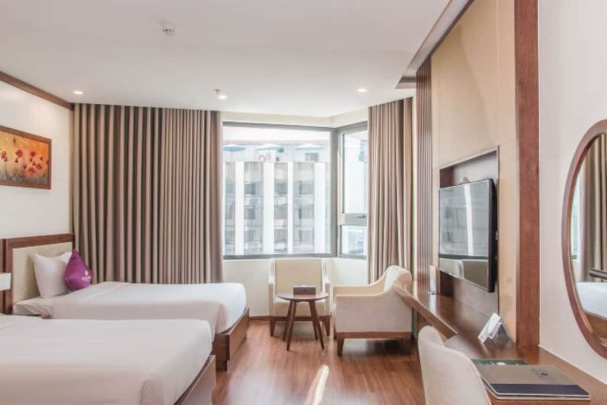 Une chambre d’hôtel avec deux lits, une télévision, un bureau, une chaise et une grande fenêtre.