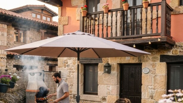 Un edificio in pietra con un balcone, zona pranzo all'aperto con sedie e tavolo, e un barbecue.