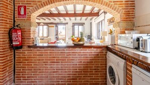 Cucina con parete in mattoni, estintore, lavatrice e una ciotola di frutta sul ripiano.
