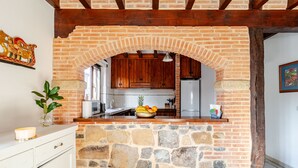 Una cucina con un arco in pietra, mobili in legno, una ciotola di frutta e un piano di lavoro bianco.
