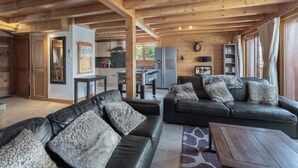 Ein gemütliches Blockhaus-Interieur mit Wohnbereich, das eine Ledersofa, einen Couchtisch, Holzbalken an der Decke und eine Küche mit modernen Geräten beherbergt.