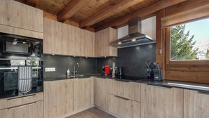 Eine moderne Küche mit Holzschränken, einer schwarzen Arbeitsplatte, Edelstahlgeräten und einem Fenster mit Blick auf Bäume.