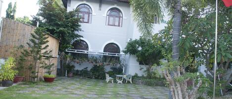 A courtyard with a white building, a bamboo fence, and potted plants.
