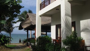 Ein Strandhotel mit einem Reetdach, einem Balkon mit Holzgeländern und Blick auf das Meer.