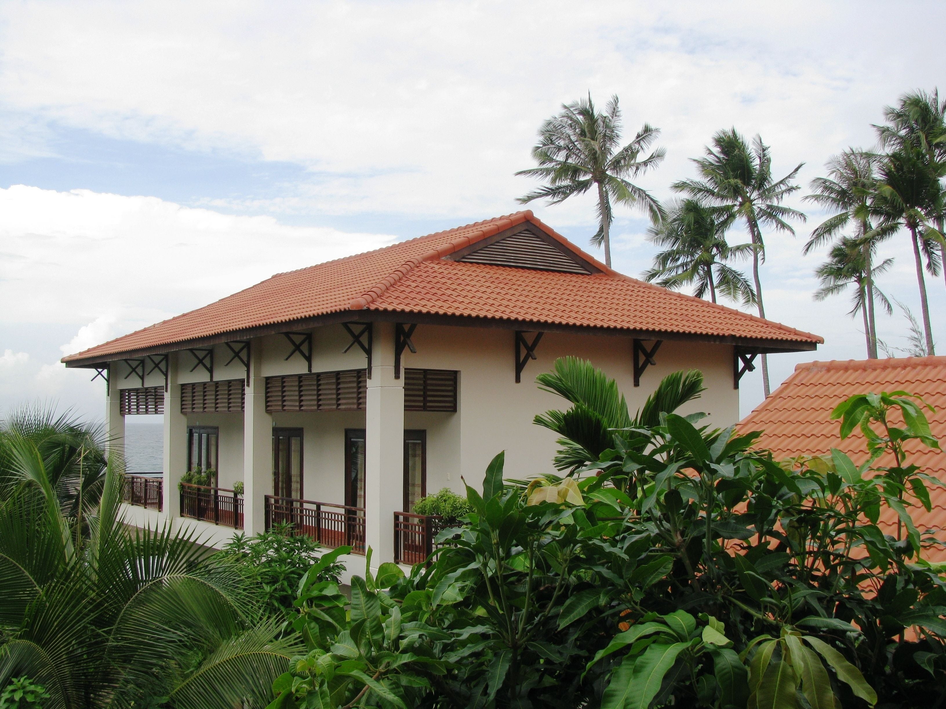 A two-story building with a red-tiled roof, white walls, and a balcony with wooden railings.