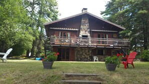 A two-story lodge with a stone chimney, a balcony with railings, and potted plants. - Chalet - MurolHouse with character (Murol)