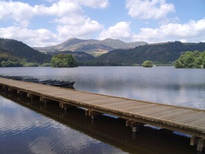 A wooden dock extending into calm water with boats lined up, surrounded by green hills and mountains under a partly cloudy sky. - Chalet - MurolHouse with character (Murol)
