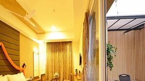 Una habitación de hotel con una cama grande, una mesita con una silla, una ventana con cortinas y vistas a un área exterior con sillas y una mesa.