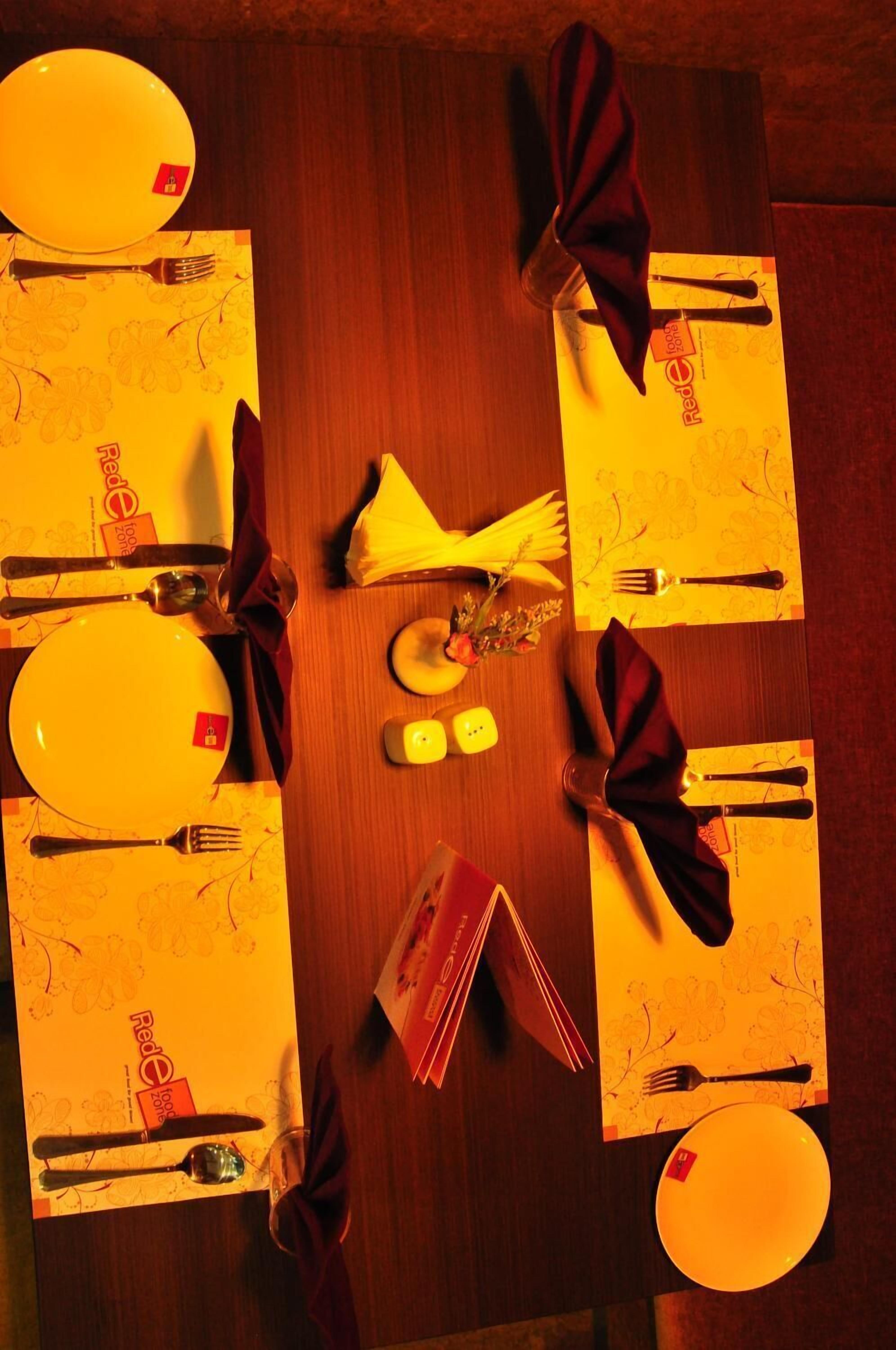 A dining table set for four with yellow placemats, red napkins, and a central vase with flowers.
