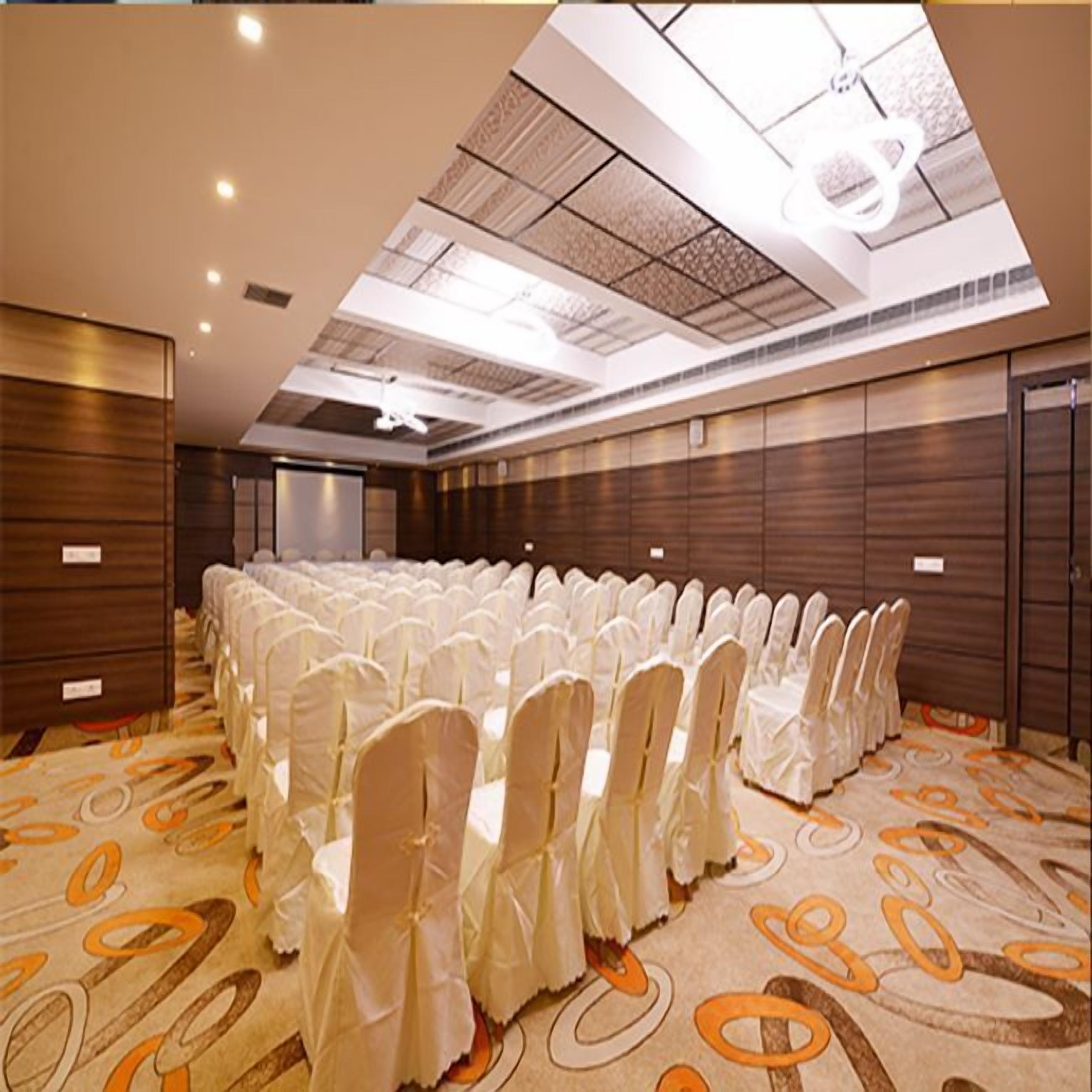 Un'ampia sala conferenze con file di sedie rivestite di bianco, una moquette decorata e un soffitto alto con lucernari.