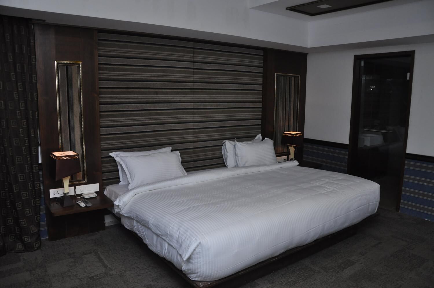 Une chambre d’hôtel moderne avec un grand lit, une tête de lit en bois foncé et deux lampes de chevet.