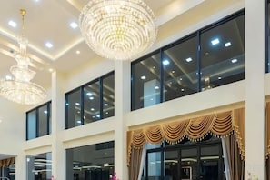 Interior de hotel con grandes ventanales, candelabros y una cortina decorativa.