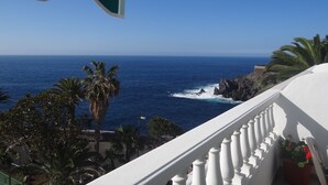 Un balcón con vista al océano, palmeras y barandilla blanca.