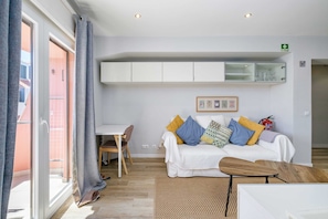 Uma sala de estar moderna com um sofá branco, uma mesa de centro de madeira e uma área de jantar com mesa e cadeiras brancas.