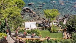 A coastal property with clear waters, rocky shoreline, and a well-maintained garden with pathways and seating areas. - AMORE RENTALS - Villa Ibiscus with Infinity Pool, Direct Sea Access, Sea View, Parking and Breakfast (Nerano)
